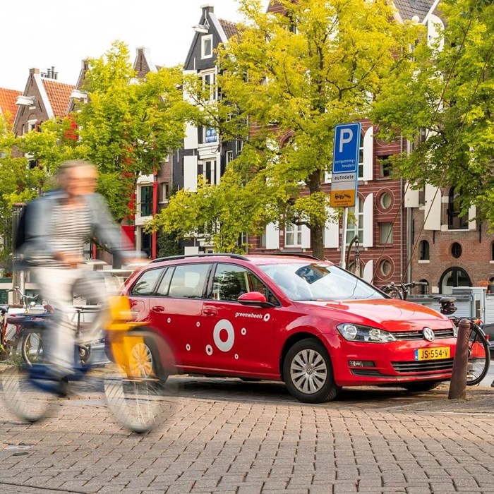 Fietser rijdt langs geparkeerde Greenwheels deelauto op straat