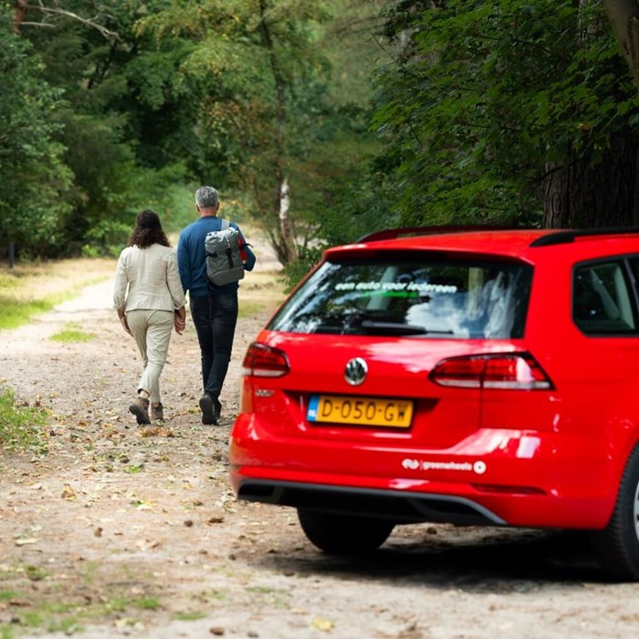 Koppel dagje uit in de natuur met rode Greenwheels auto