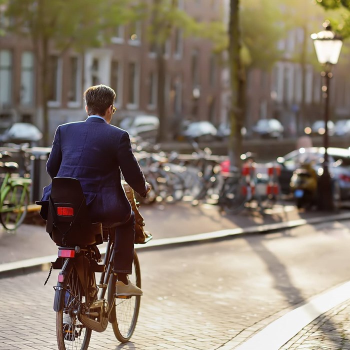 Zakelijke man fietst in Amsterdam met kinderzitje door stad vierkante afbeelding