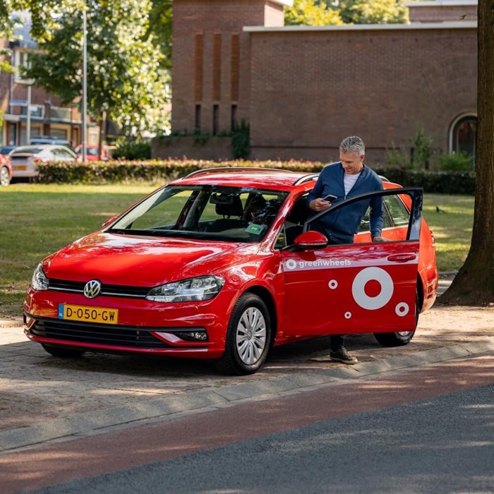 Man stapt in rode Greenwheels deelauto op straat