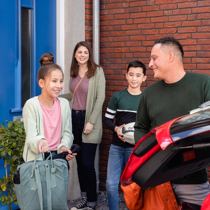 Familie laadt bagage in rode Greenwheels deelauto