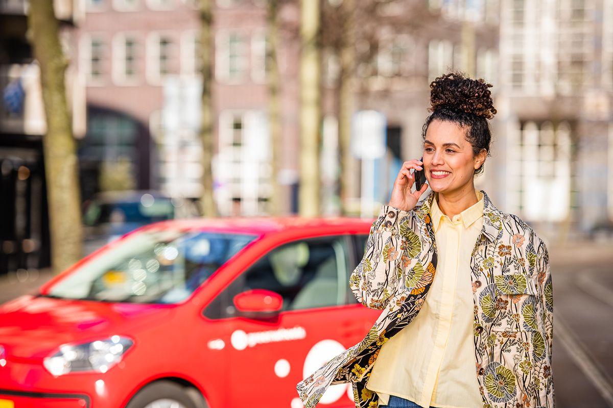 Greenwheels Deelauto geparkeerd jonge vrouw met mobiel zakelijk