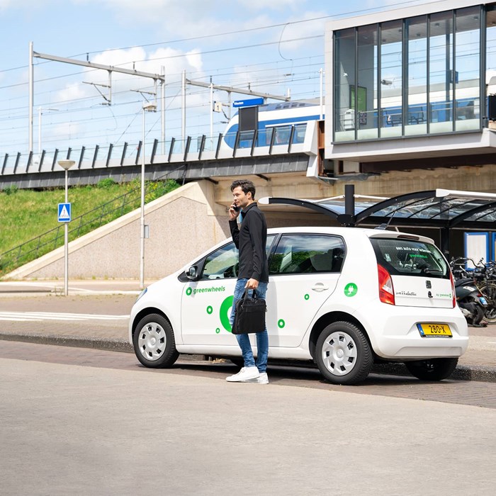 Man belt bij elektrische Greenwheels deelauto bij treinstation