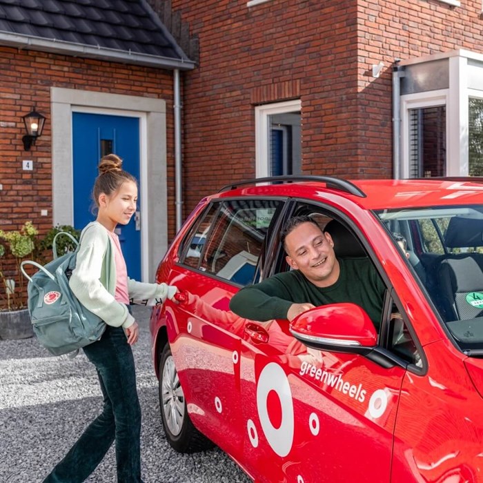 Vader en kind stappen in rode Greenwheels auto