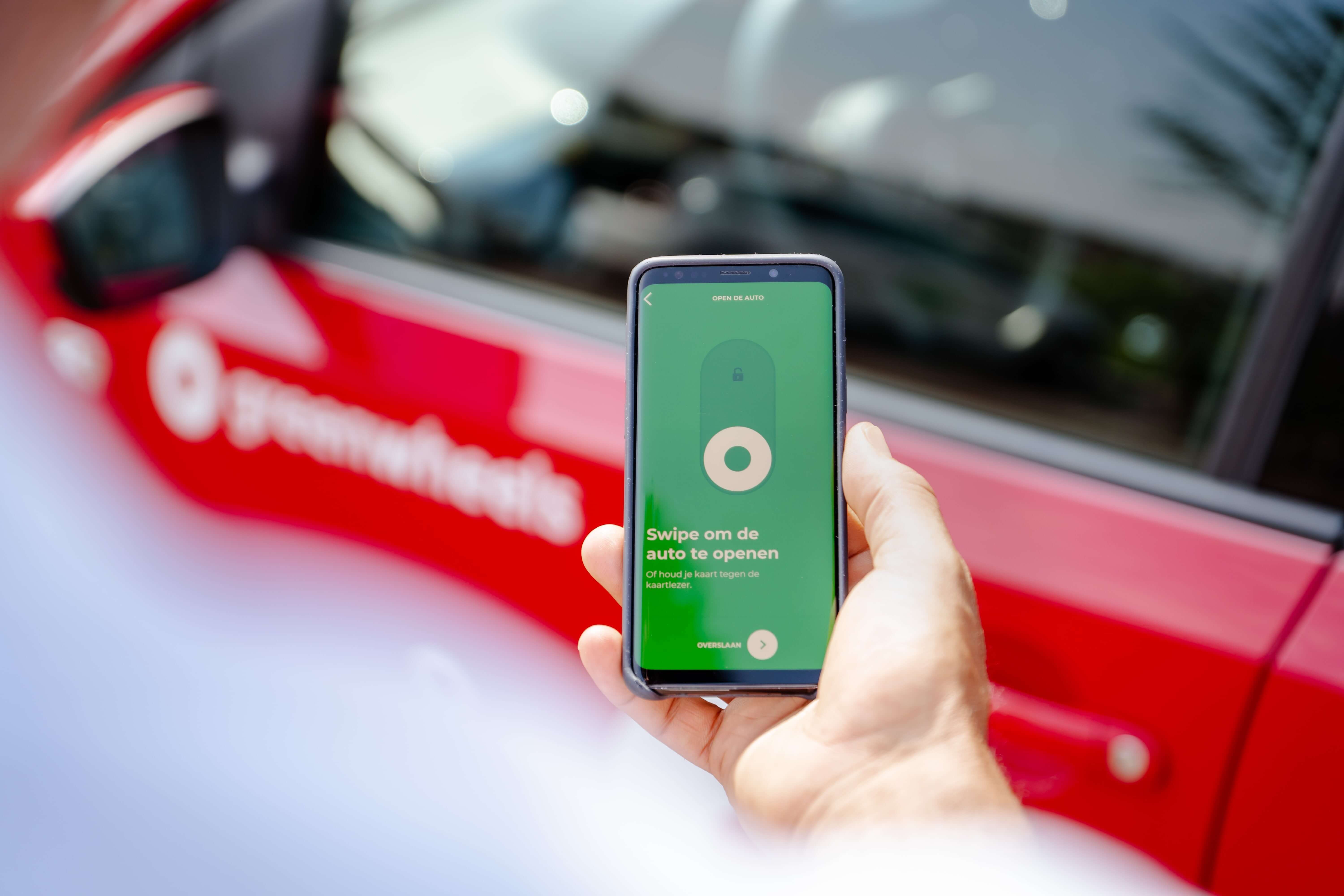 Greenwheels auto openen met app telefoon in hand deelauto op achtergrond
