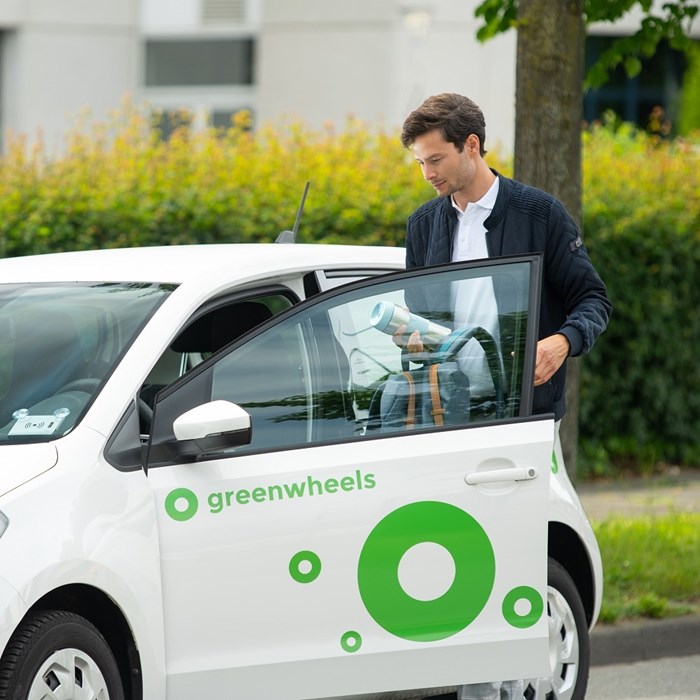 Man stapt in elektrische Greenwheels deelauto langs de weg