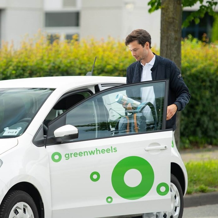 Man stapt in witte elektrische Greenwheels auto langs de weg