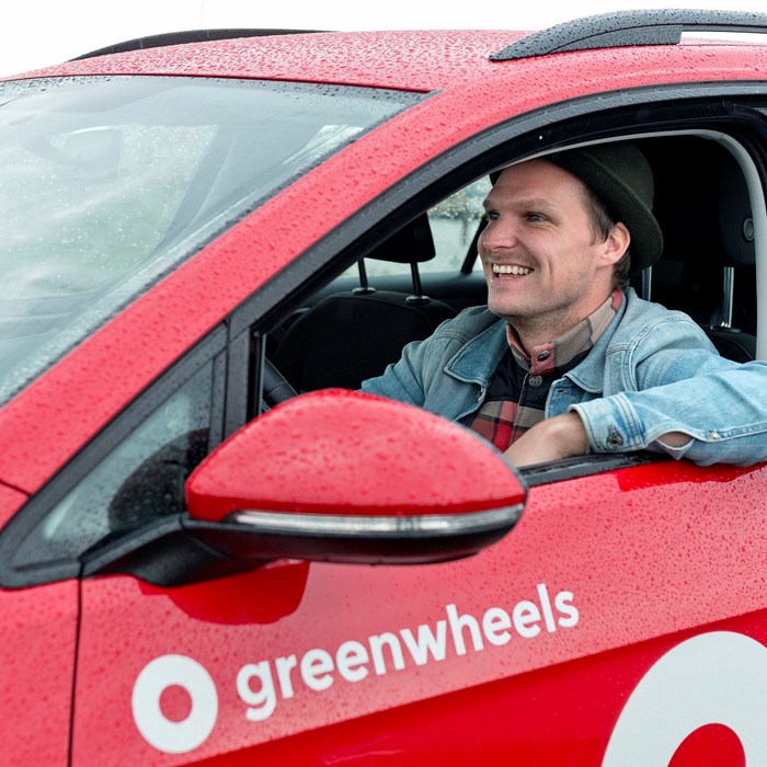 Autodelen jongeman regen op auto Greenwheels bestuurder deelauto