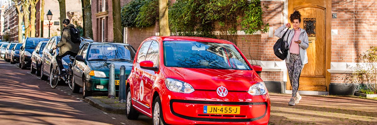 Vrouw loopt naar rode Greenwheels deelauto