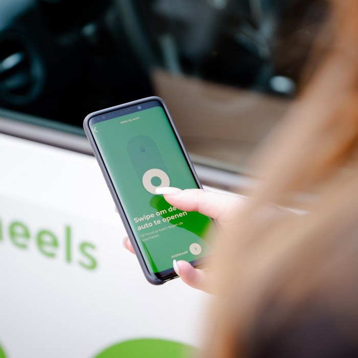Vrouw gebruikt Greenwheels app swipe om te openen met rechterhand bij elektrische auto