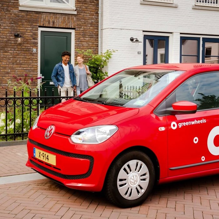 Man en vrouw met rode Greenwheels deelauto