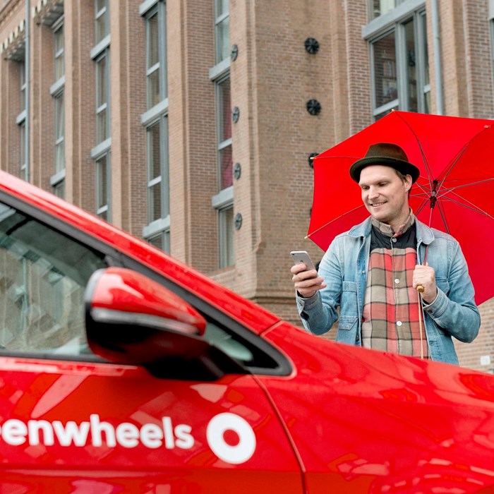 Man in regen naast rode Greenwheels deelauto
