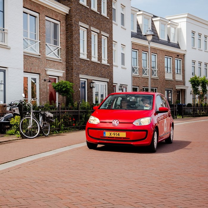 Koppel rijdt in rode Greenwheels deelauto in woonwijk