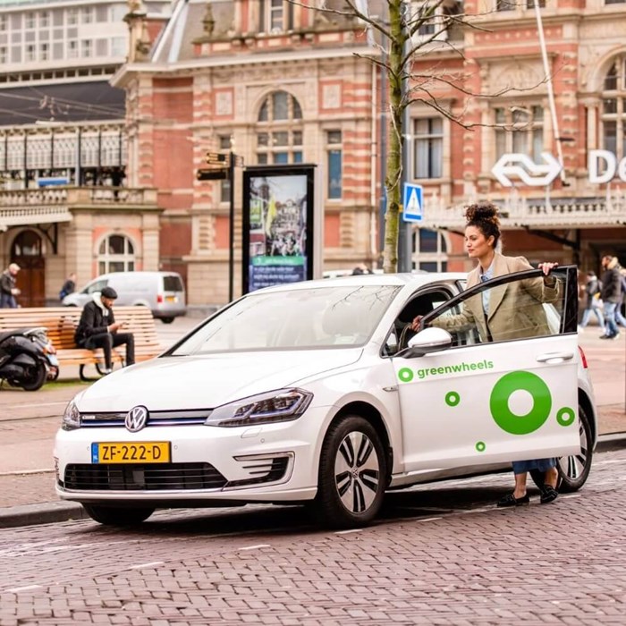 Vrouw stapt in witte elektrische Greenwheels auto op NS station