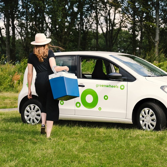 Dame met koelbox bij elektrische Greenwheels auto op gras voor picknick